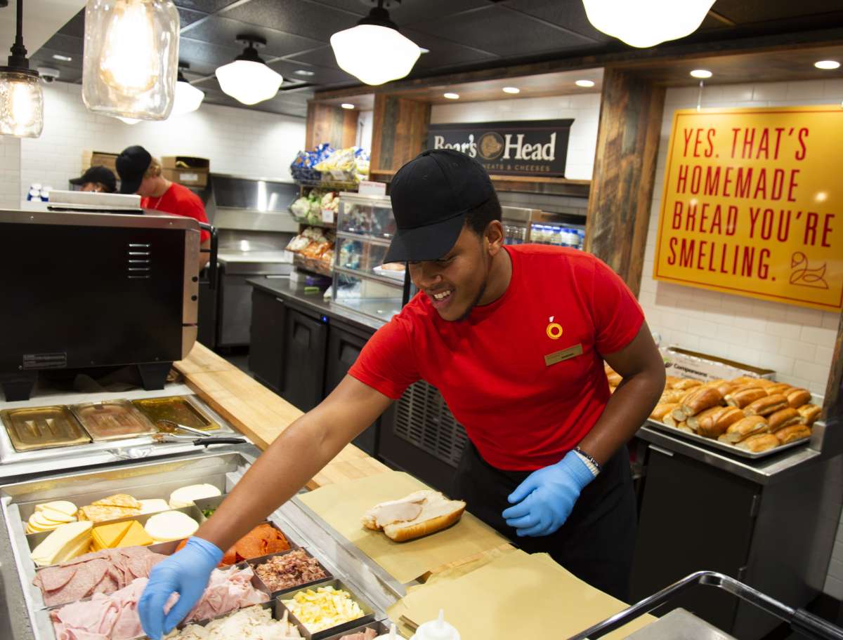 Male employee making a sandwich and smiling.